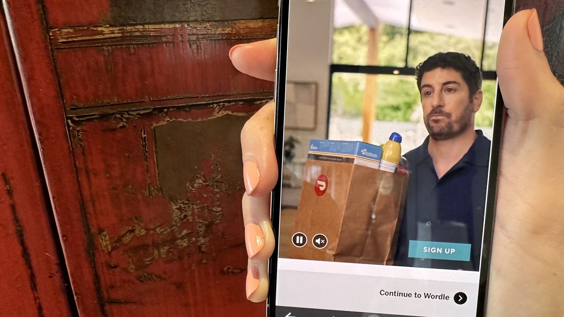 Image of a hand holding an iPhone with the DoorDash ad running on the NYTimes.com's Wordle site that features Jason Biggs