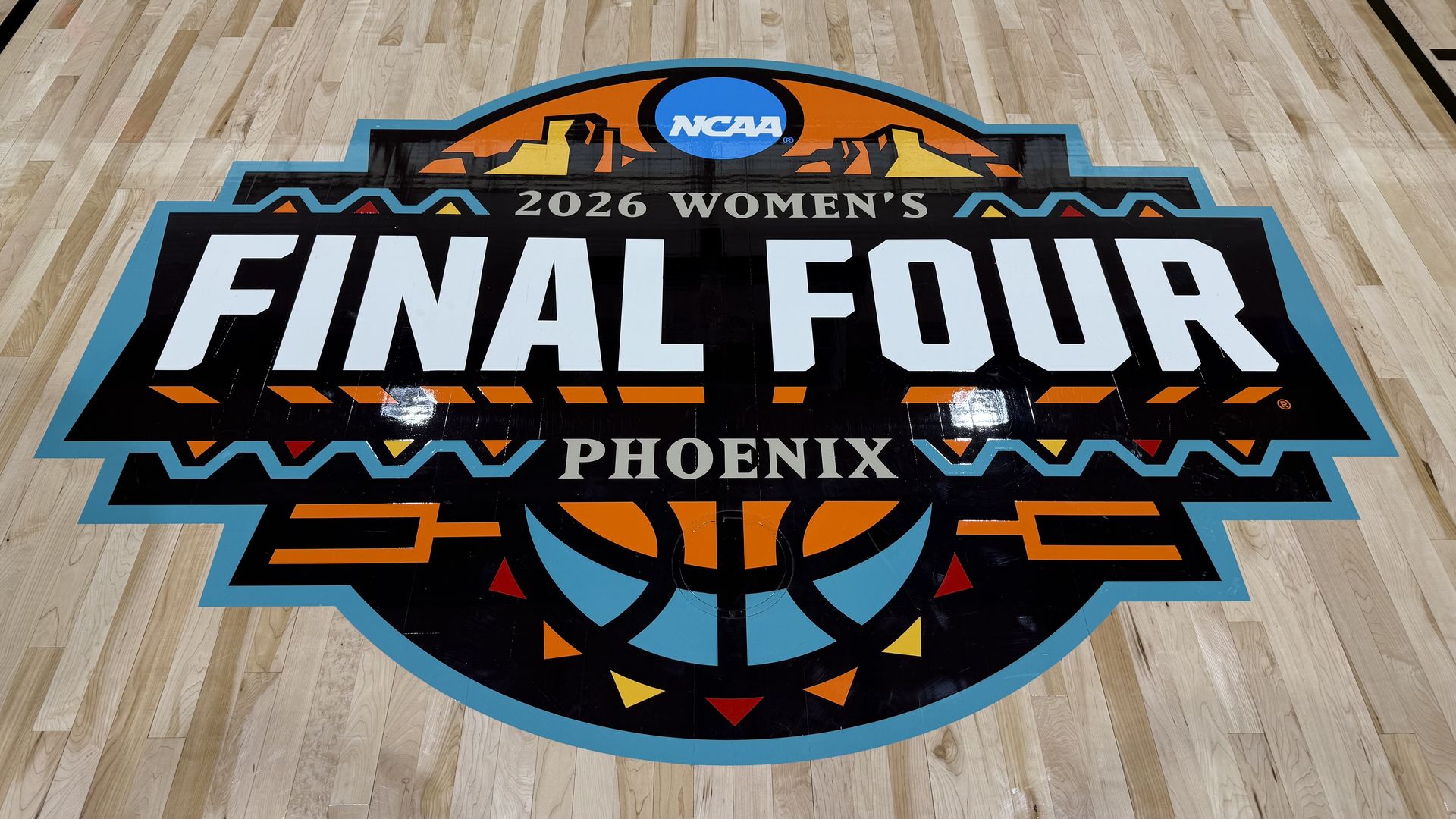 Colorful NCAA Final Four logo painted on a basketball court, reading "2026 Women's Final Four" with "Phoenix" beneath; blue border, orange and yellow mountains, and a basketball motif.