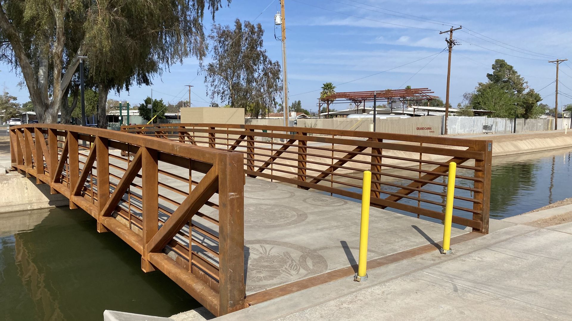 A concrete walkway with rust-colored metal railings going over a canal. 