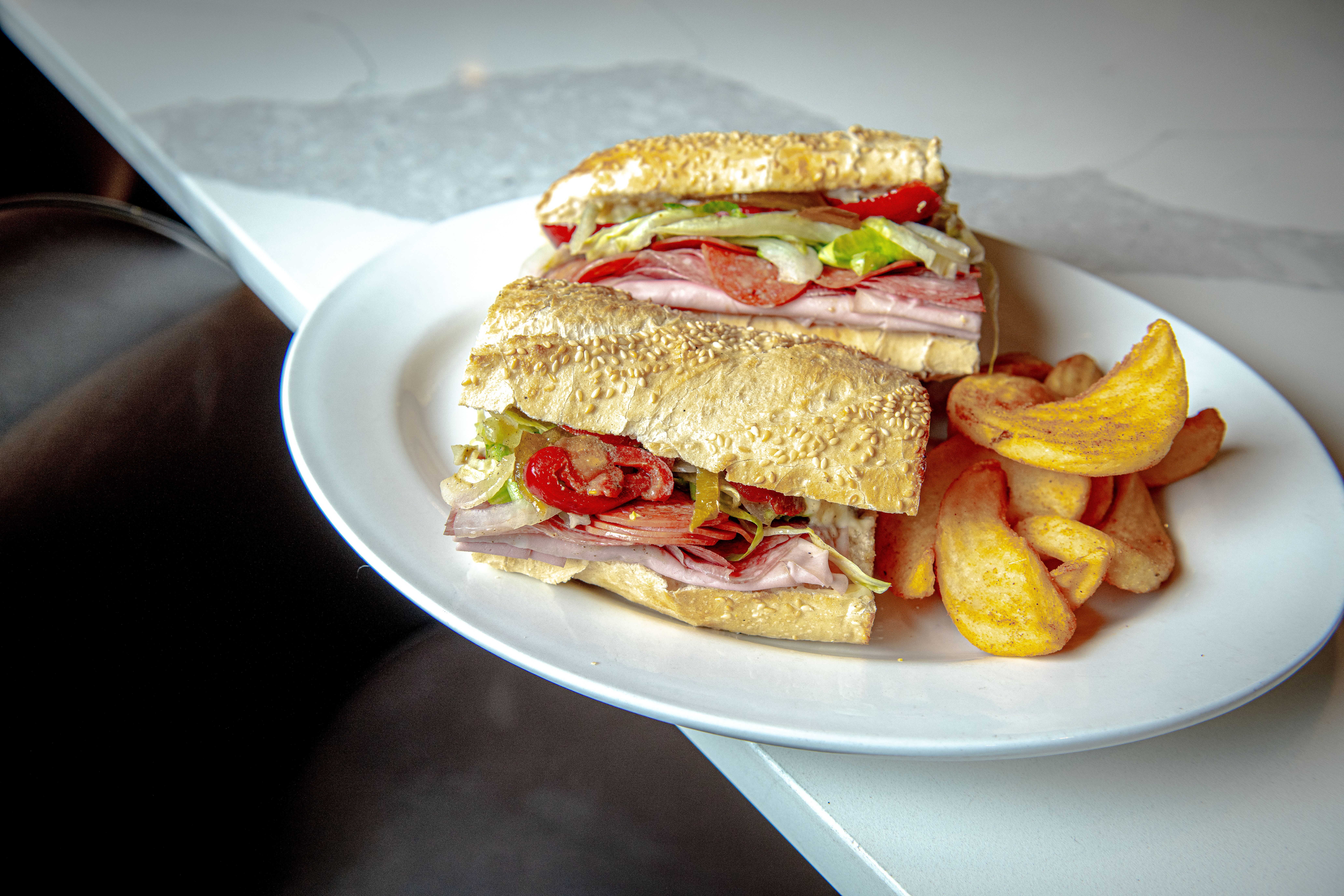 An Italian sandwich on a seeded bun with lettuce, tomato and fries on the side