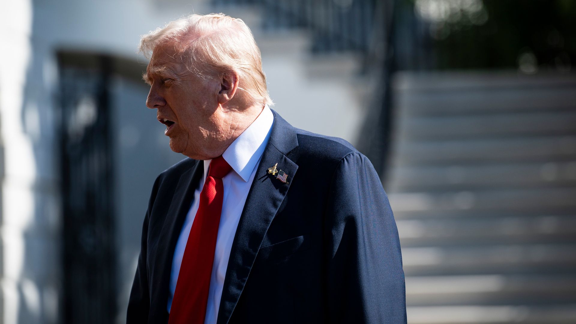 Trump, seen from the side wearing a dark suit and a red tie, speaks to reporters (not pictured) outside the White House.