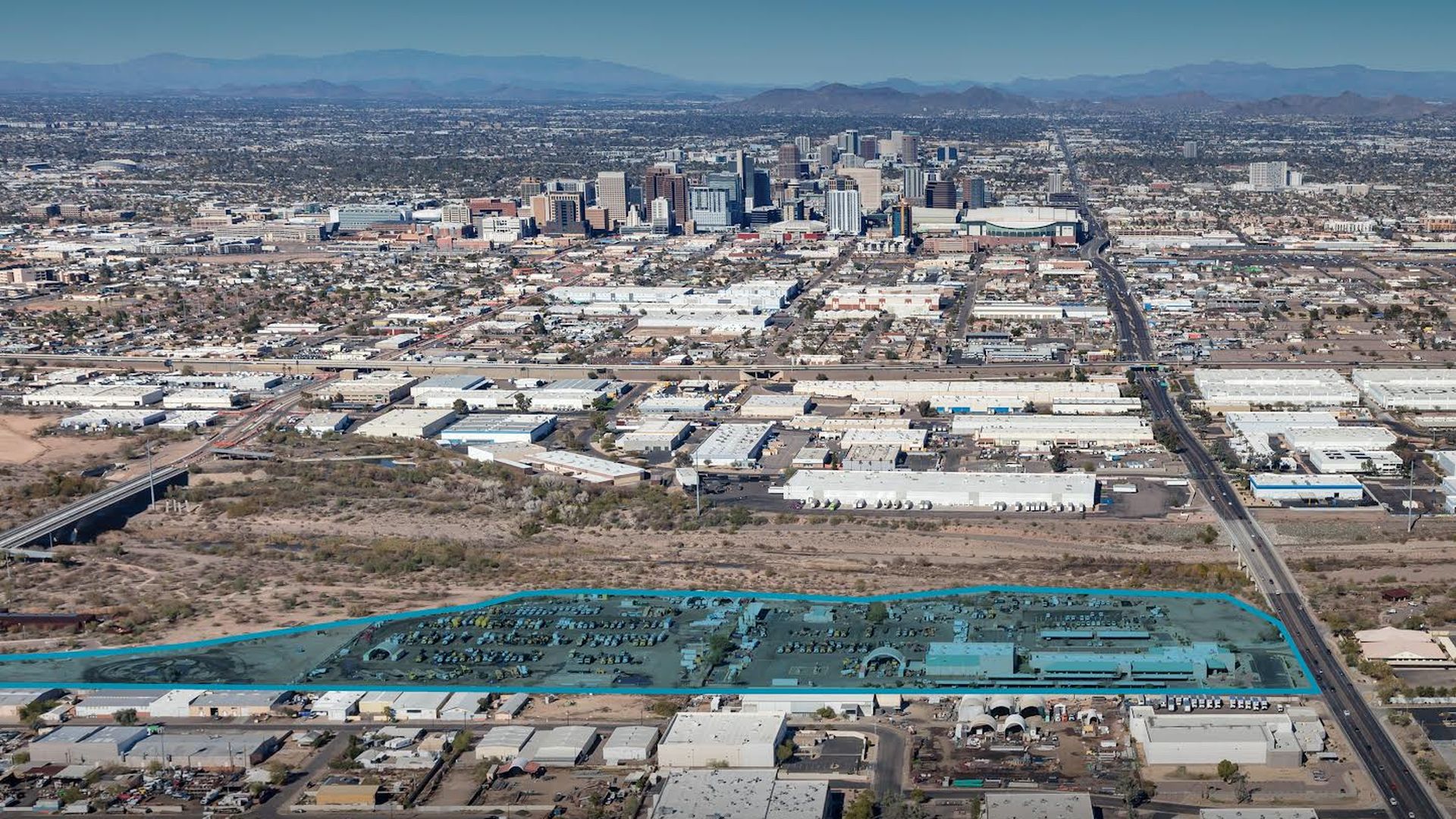 An aerial of Phoenix looking toward downtown from the south, with a swath of land along a dry riverbed highlighted in blue. 