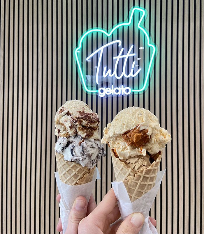 Gelato cones in front of a lit up "Tutti Gelato" sign.