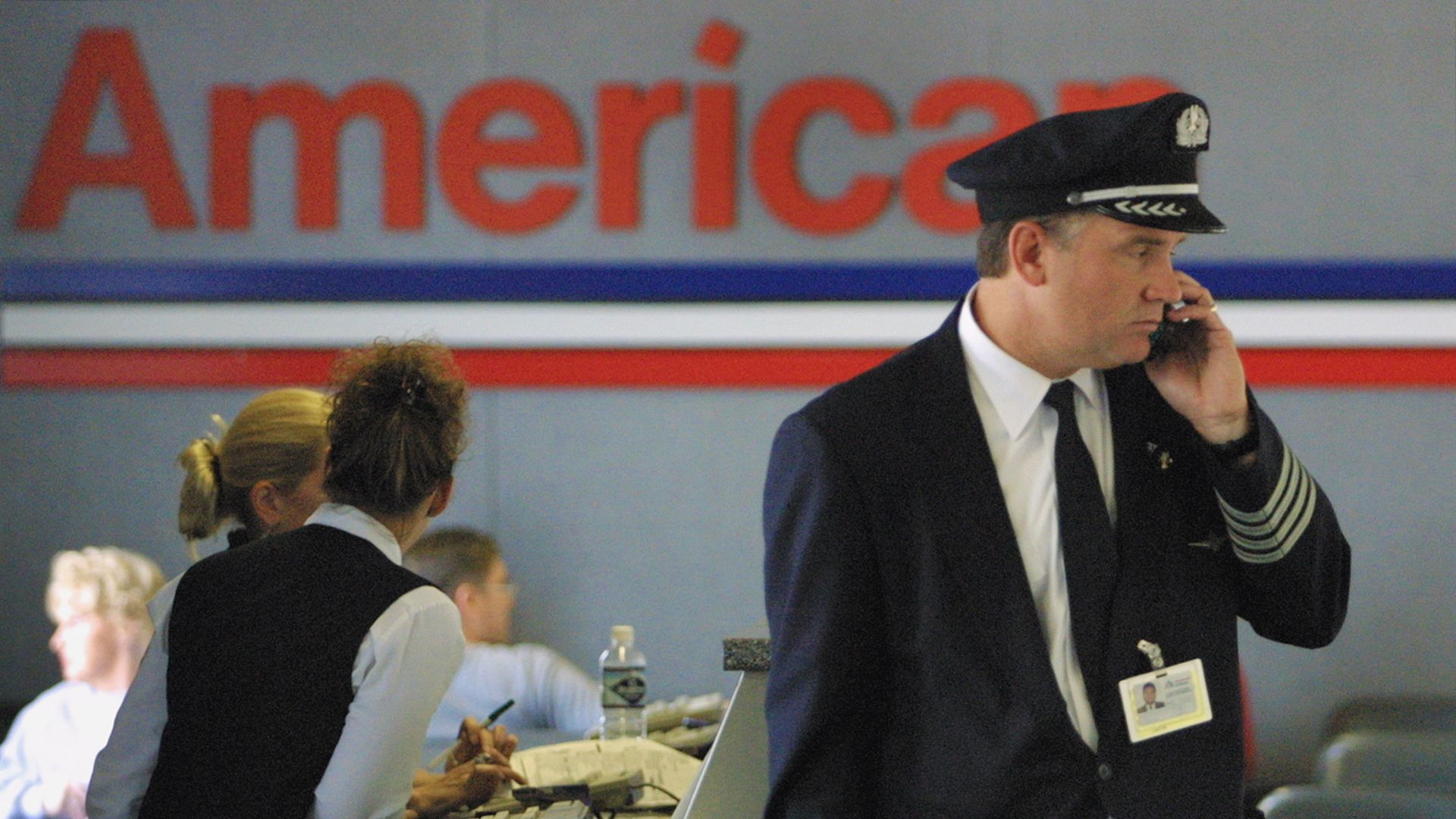A pilot talks on the phone in front the American Airlines logo and two gate workers