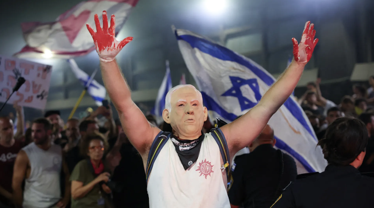 A protester in Tel Aviv, wearing a mask depicting Israel's Prime Minister Benjamin Netanyahu, raises his hands wearing gloves with red paint, during an anti-government rally calling for the release of Israelis held hostage by Hamas militants in Gaza since October on Sunday, Sept. 1.