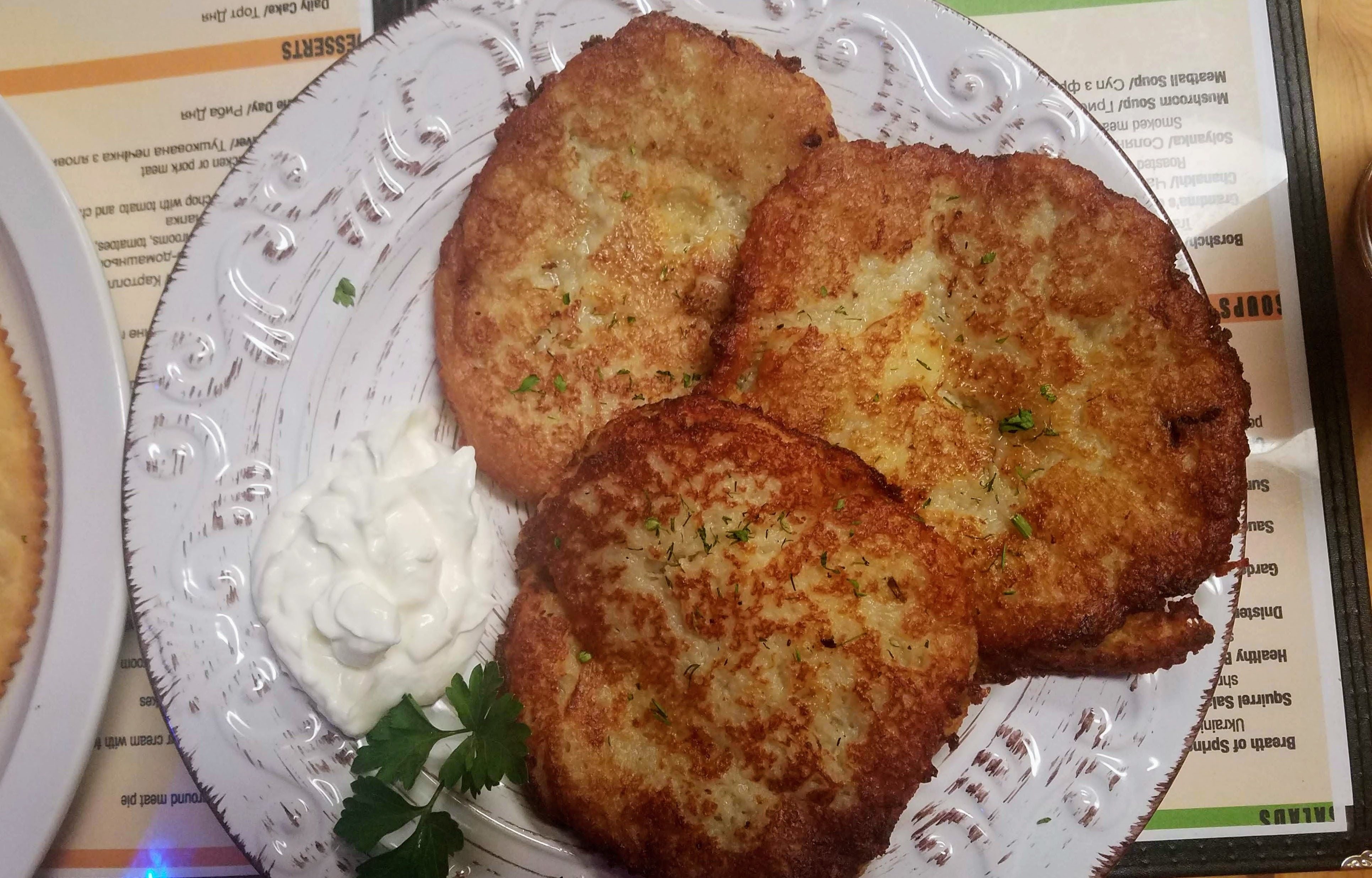A plate of three latkes with sour cream on the side.