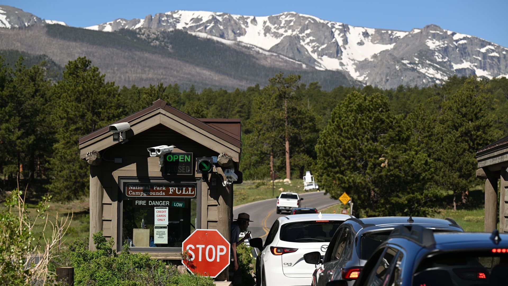 Cars line up at the Beaver Meadows entrance of the Rocky Mountain National Park, with snow-capped mountains in the background.