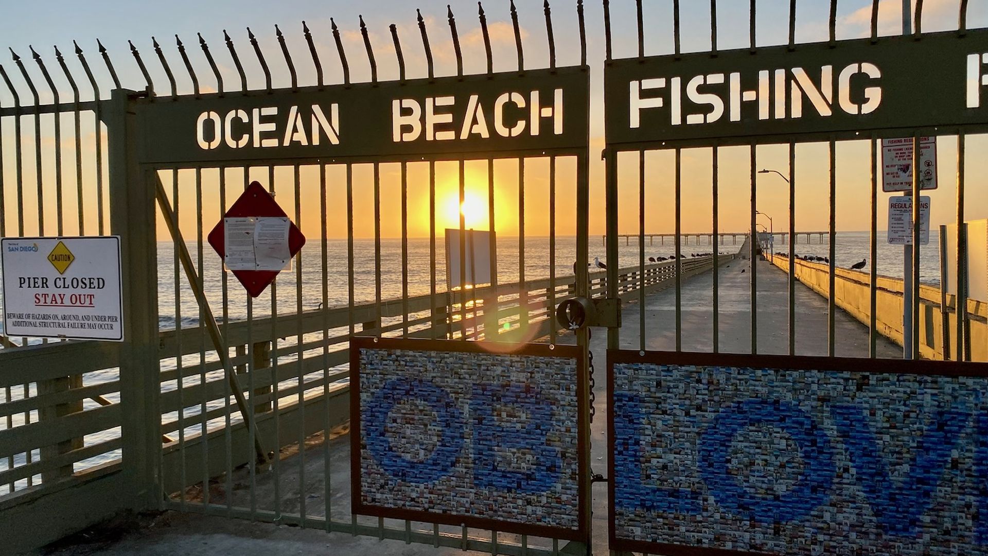 A closed gated entrance to a pier at sunset.