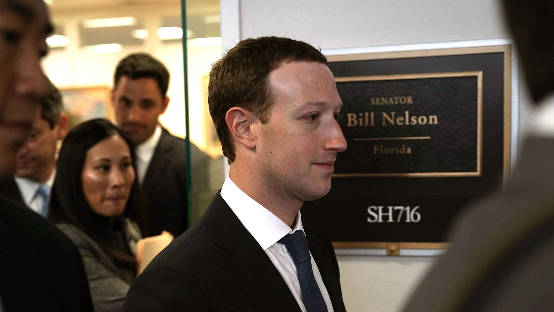Facebook CEO Mark Zuckerberg walks by a sign for Bill Nelson's office