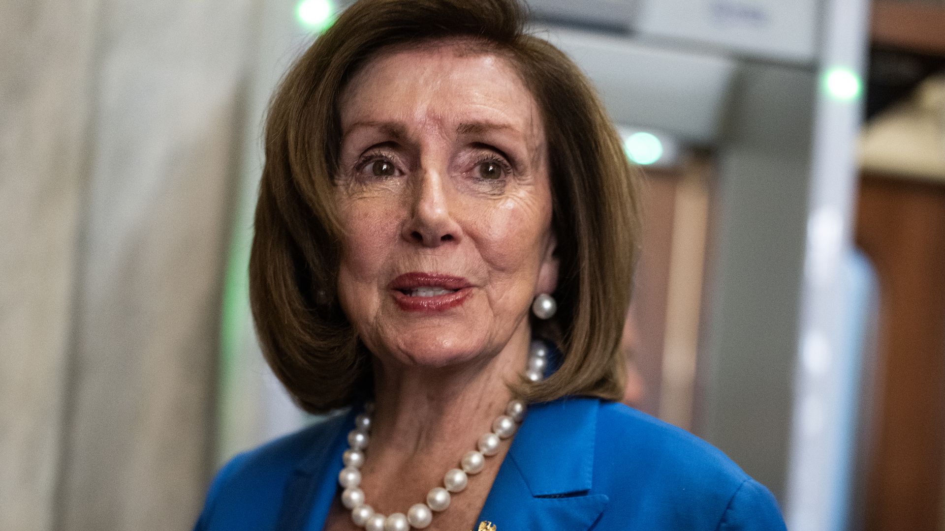 Former House Speaker Nancy Pelosi, wearing a blue suit in front of a metal detector.