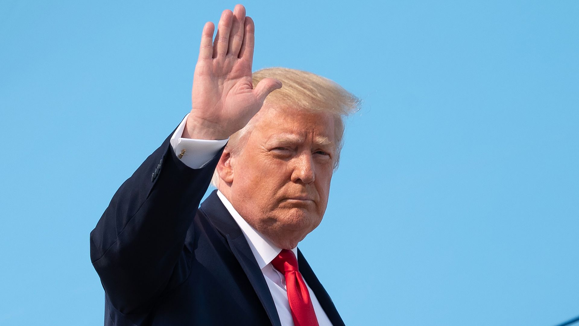 Trump wears a suit and waves at the camera