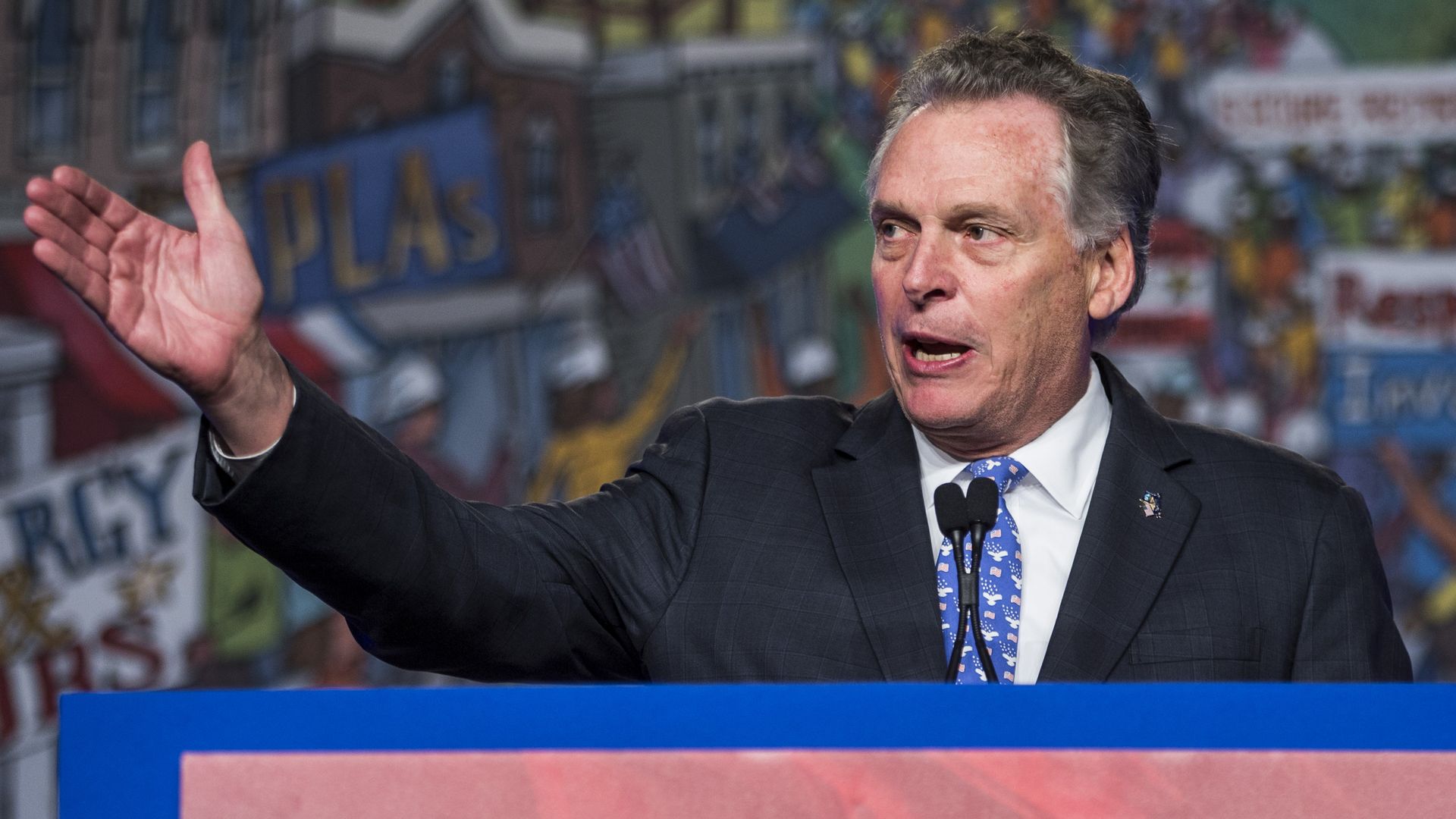 In this image, McAuliffe stands and gestures at a podium while speaking.