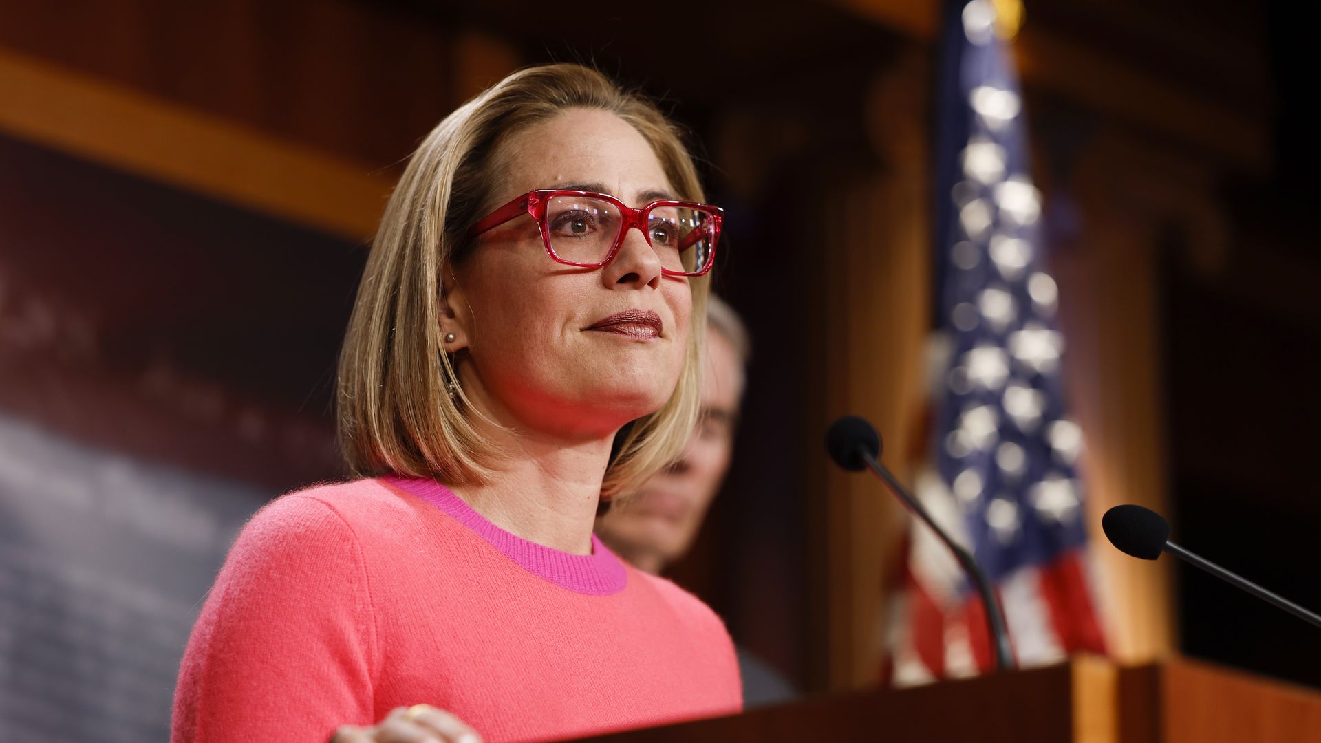 Kyrsten Sinema stands in front of a microphone at a lectern