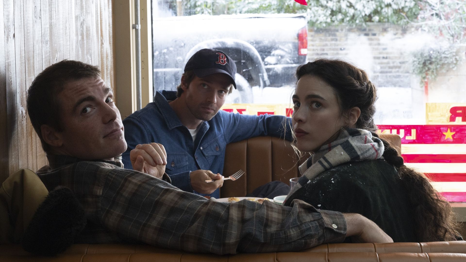 Three people (played by Gabriel Basso, Patrick Schwarzenegger and Margaret Qualley) sit in a booth inside a casual diner. Left man in plaid leans back, center man wears a navy cap and denim shirt, and right woman with a scarf looks toward the camera.