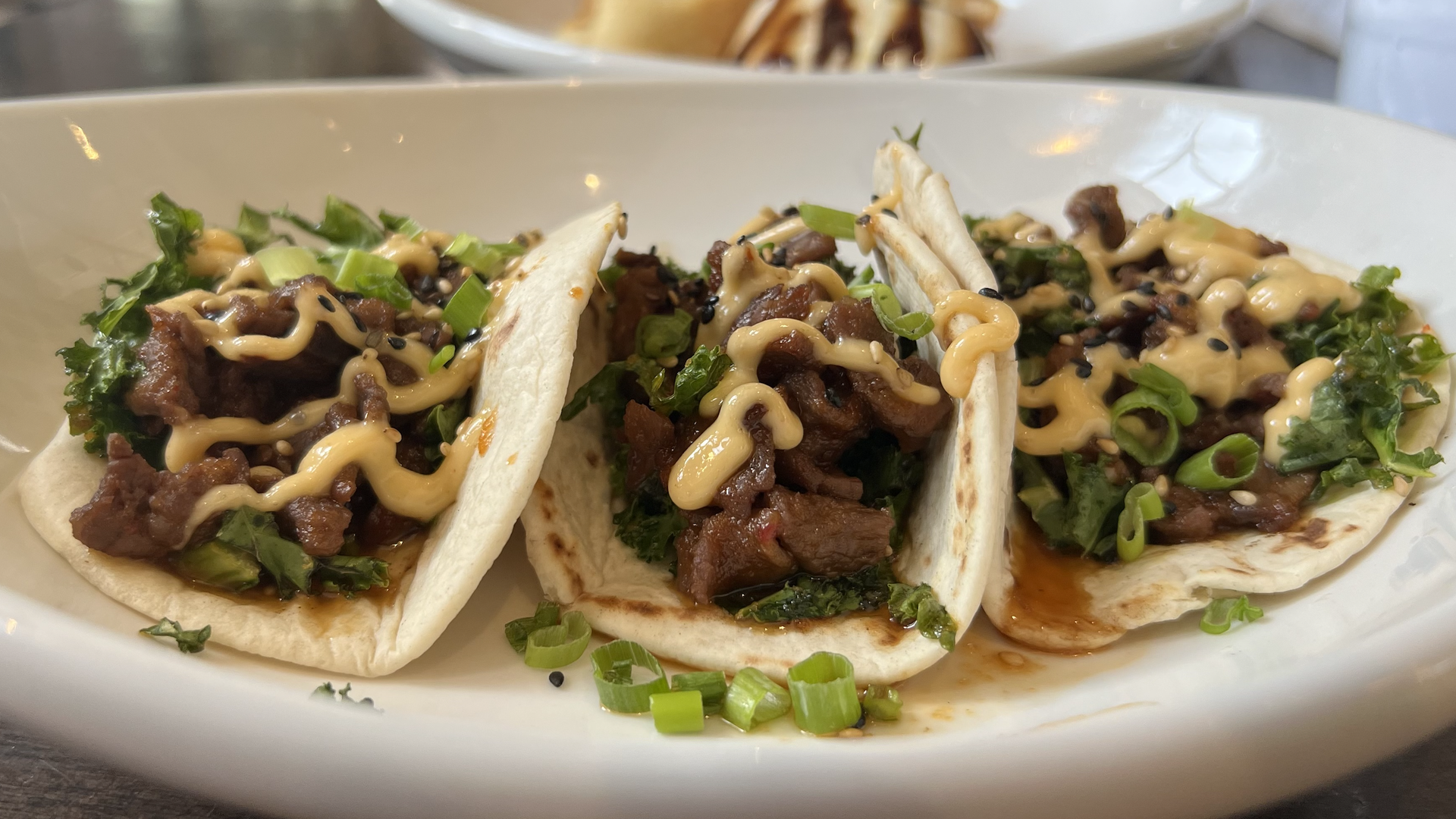 Three beef tacos with a sauce drizzled on them and green onions