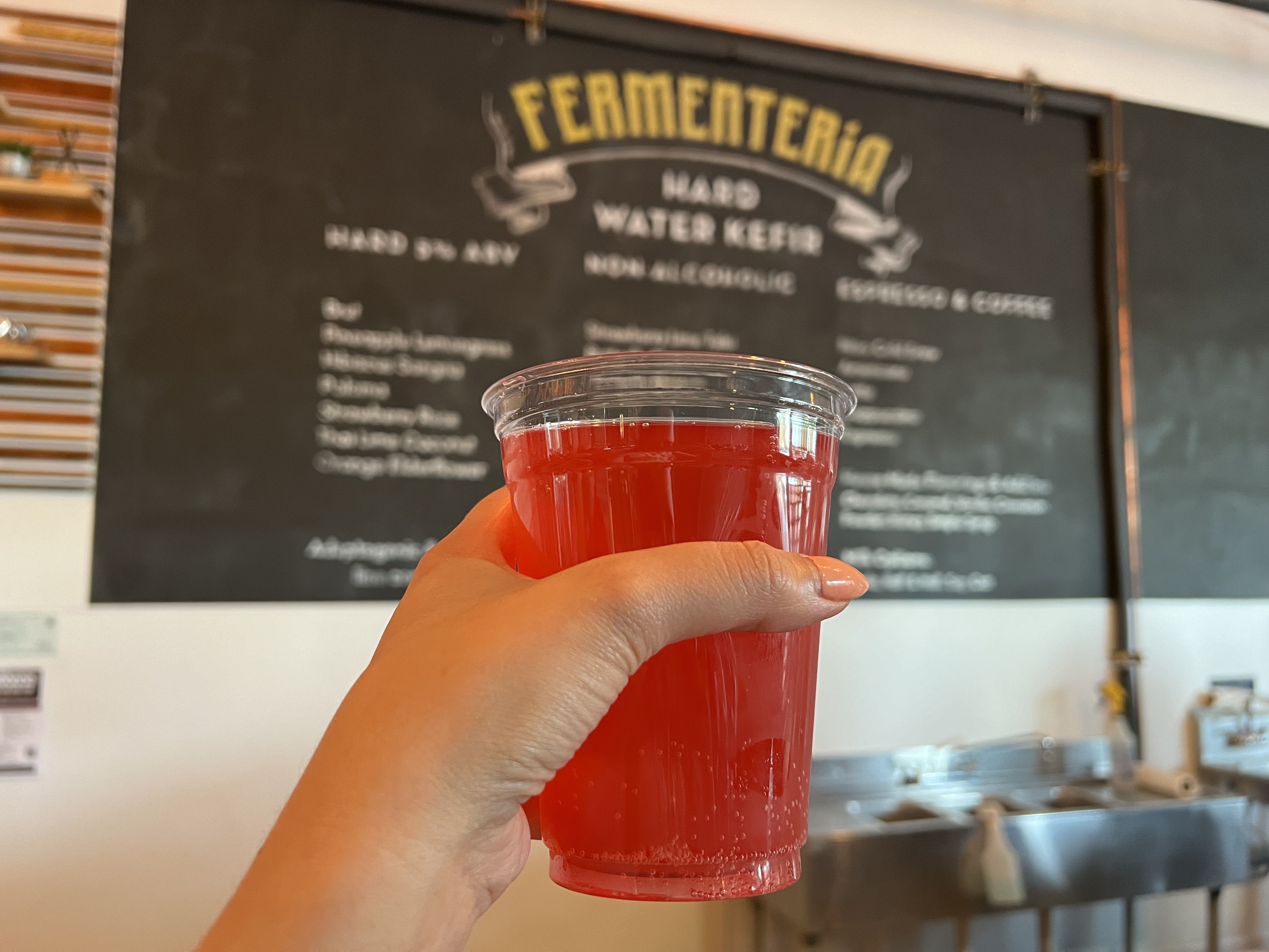 A hand holds up a plastic cup of kefir that's pink-orange in color.