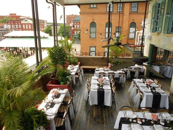 a rooftop patio with tables, fans and plants overlooking a market