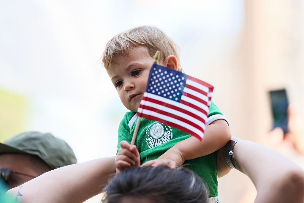 A child sitting on an adults shoulder's holds a small American flag.