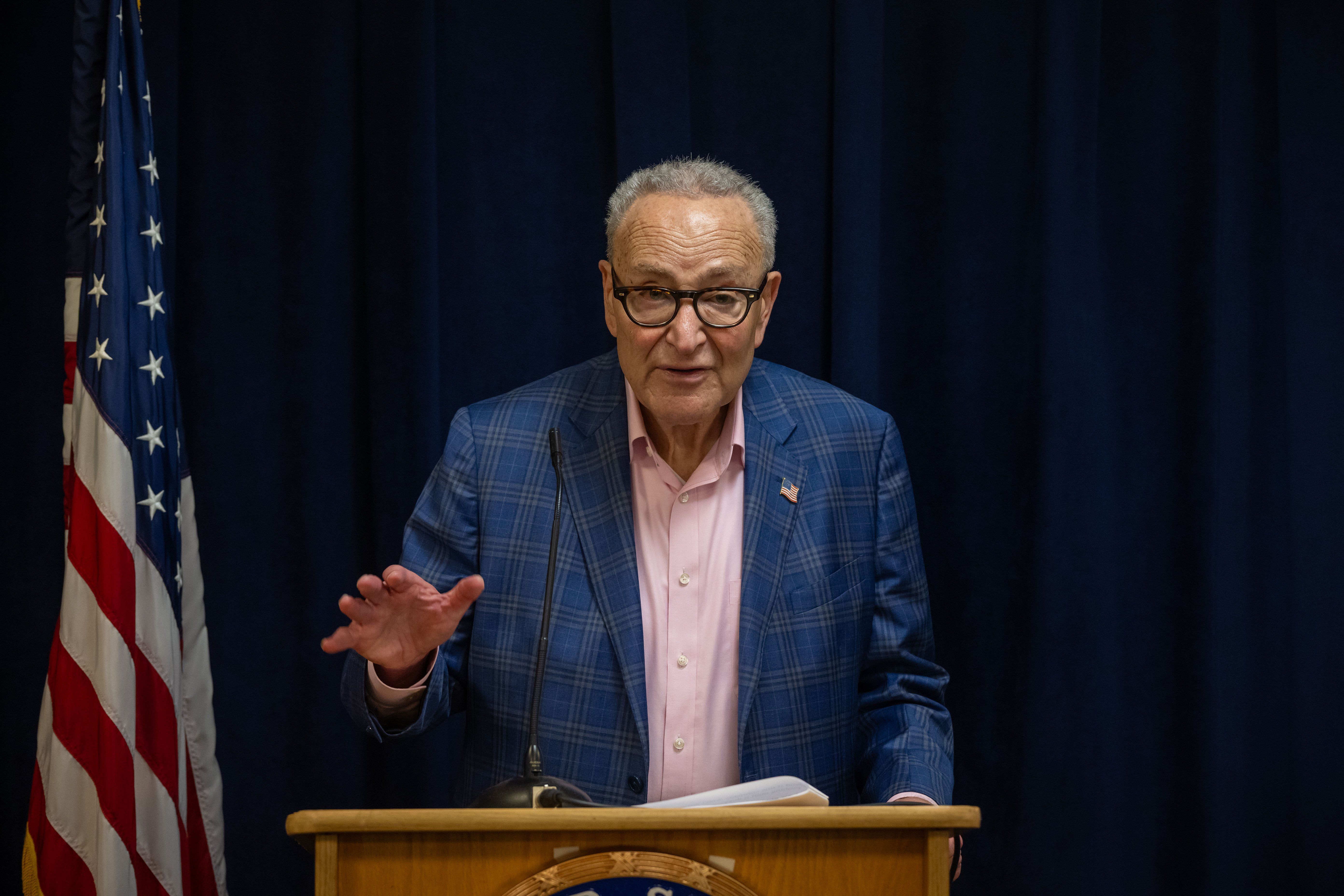 Tieless Schumer at podium with flag