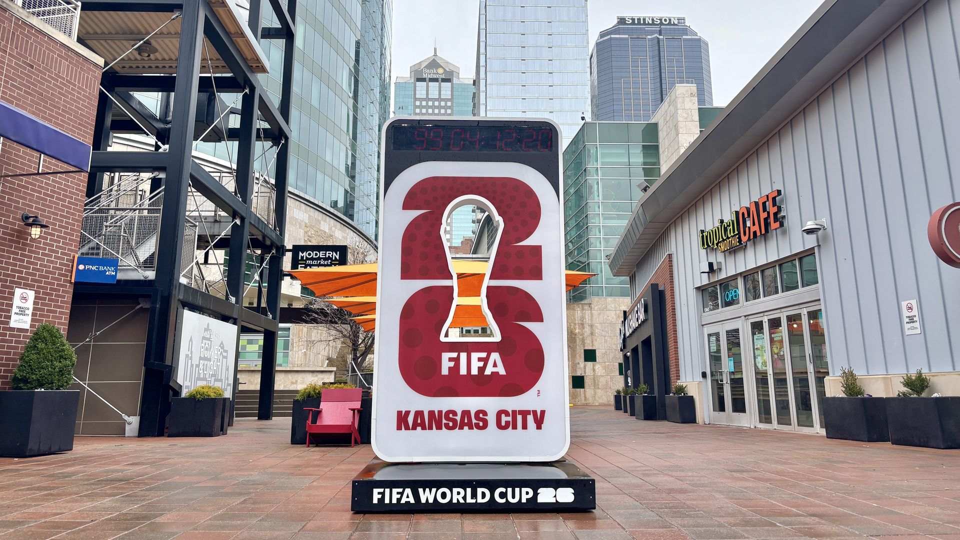 Countdown clock for FIFA World Cup 2026 in Kansas City, featuring a red and white design with a stylized trophy silhouette and city buildings in the background.