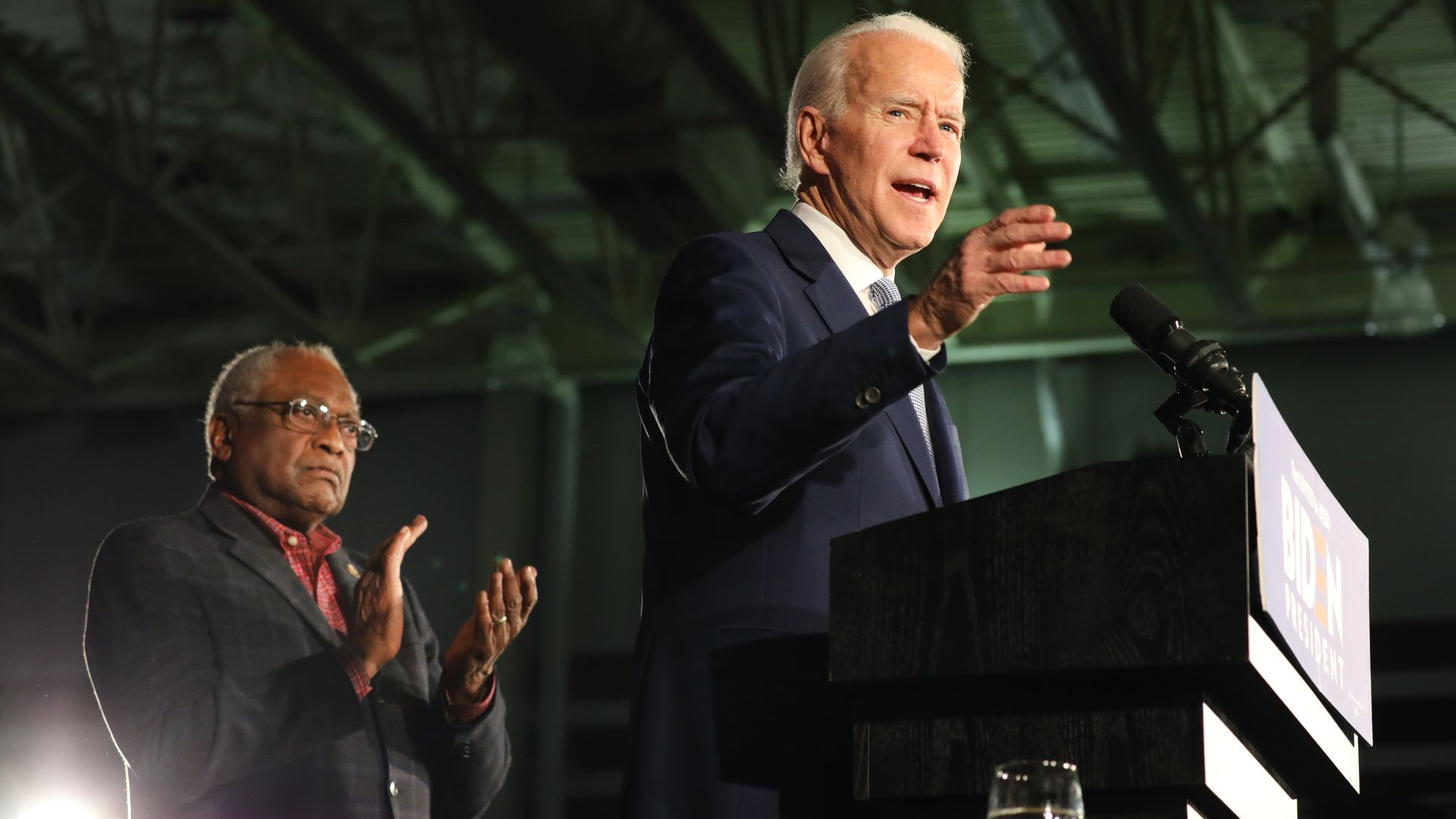 In this image, Clyburn stands behind Biden. Biden stands at a podium.