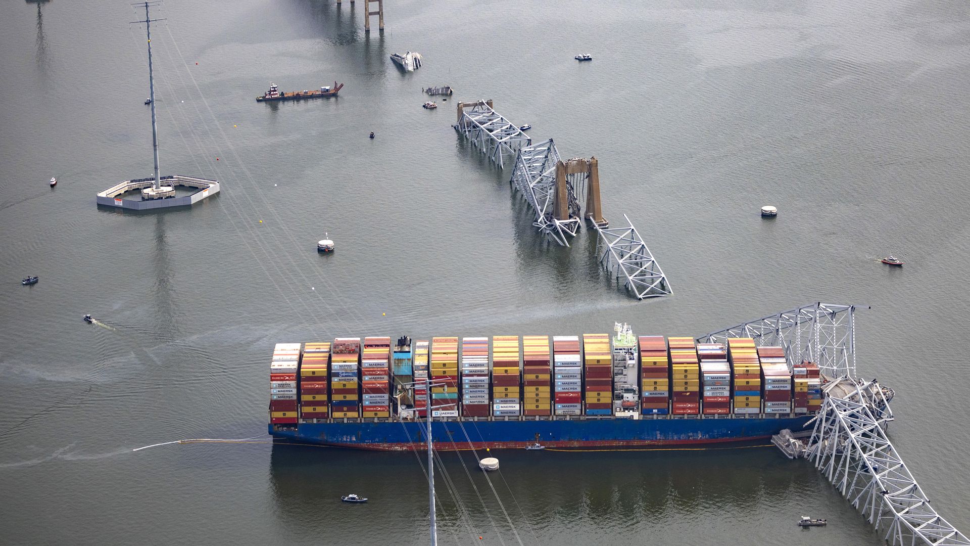 A cargo ship sits in the water facing a broken bridge.