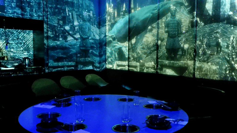 Animated image of a round table surround by Screen that looks like it's underwater with a whale 