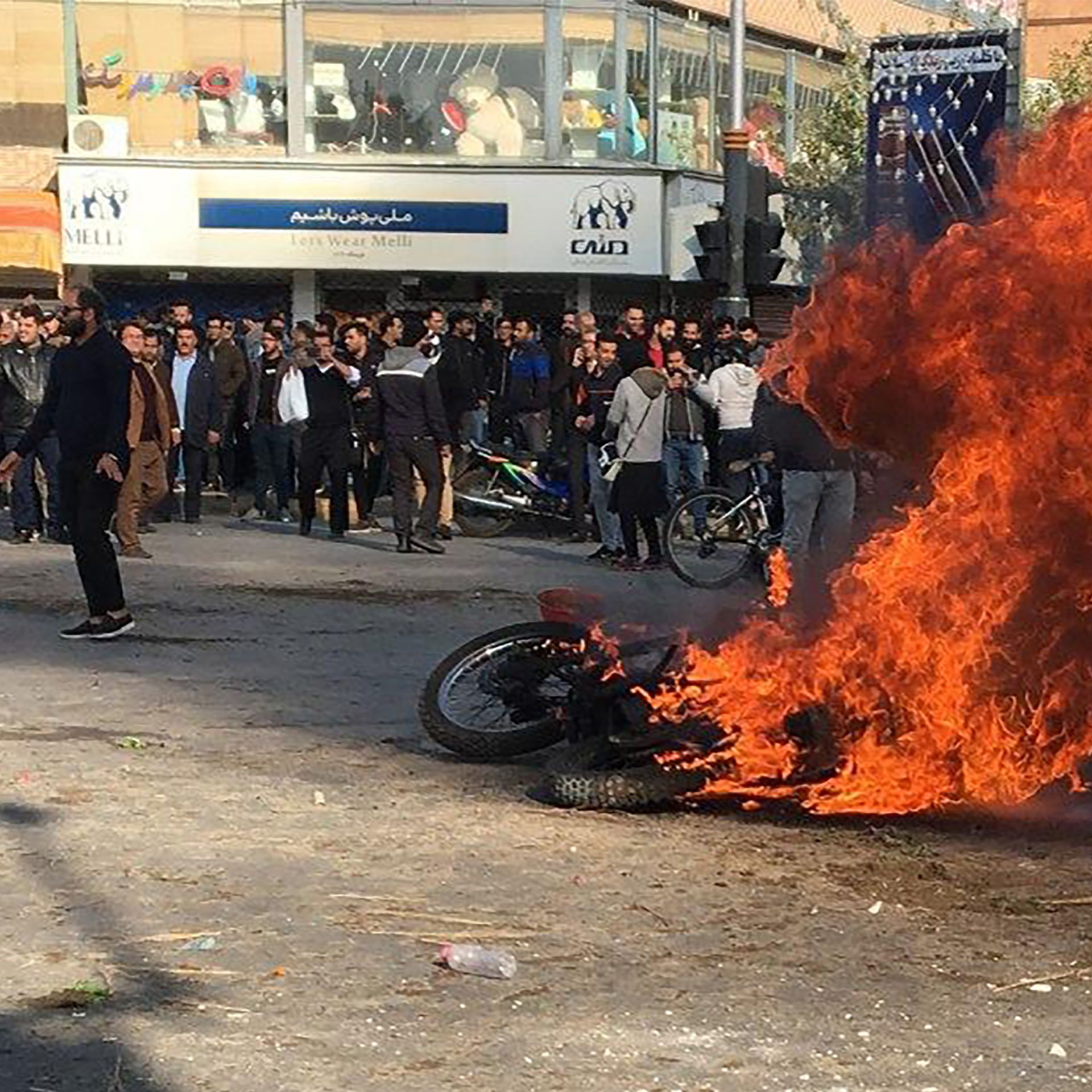 protestors surround a burning motorcycle in a street intersection