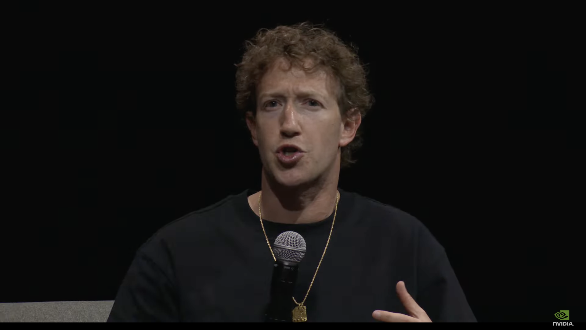 photo of Mark Zuckerberg wearing a black T-shirt and gold chain holding a mic talking on stage