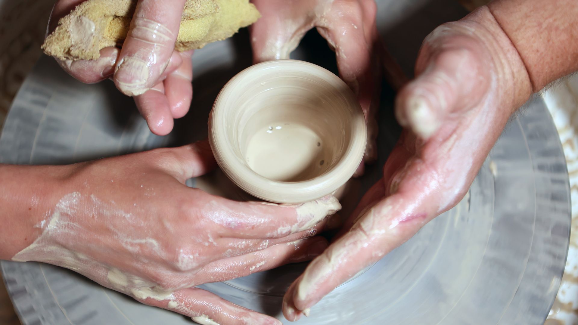 Hands around a pottery wheel and bowl.