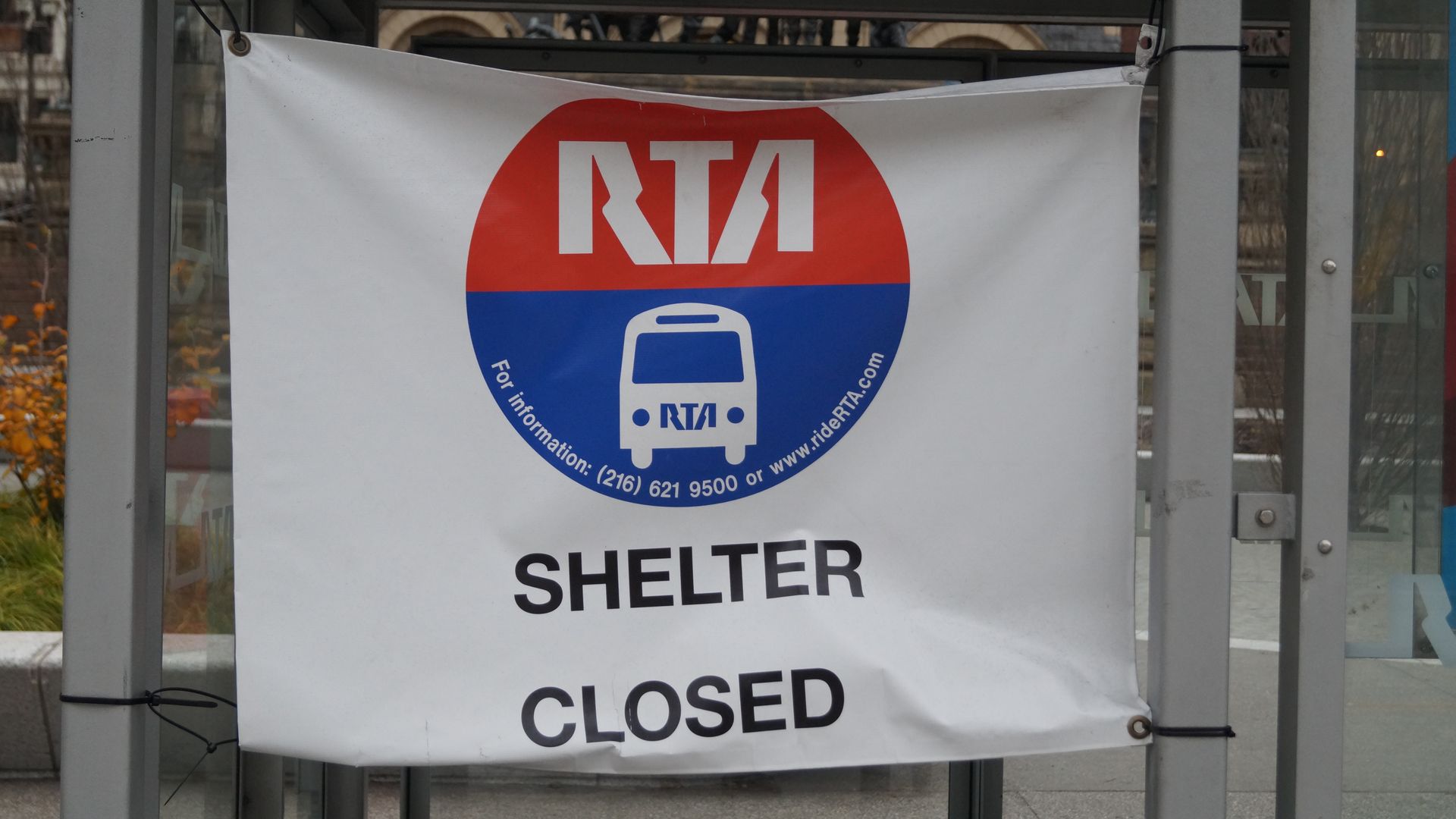 White banner with red and blue RTA logo says "SHELTER CLOSED" at a bus shelter structure in an outdoor urban area.