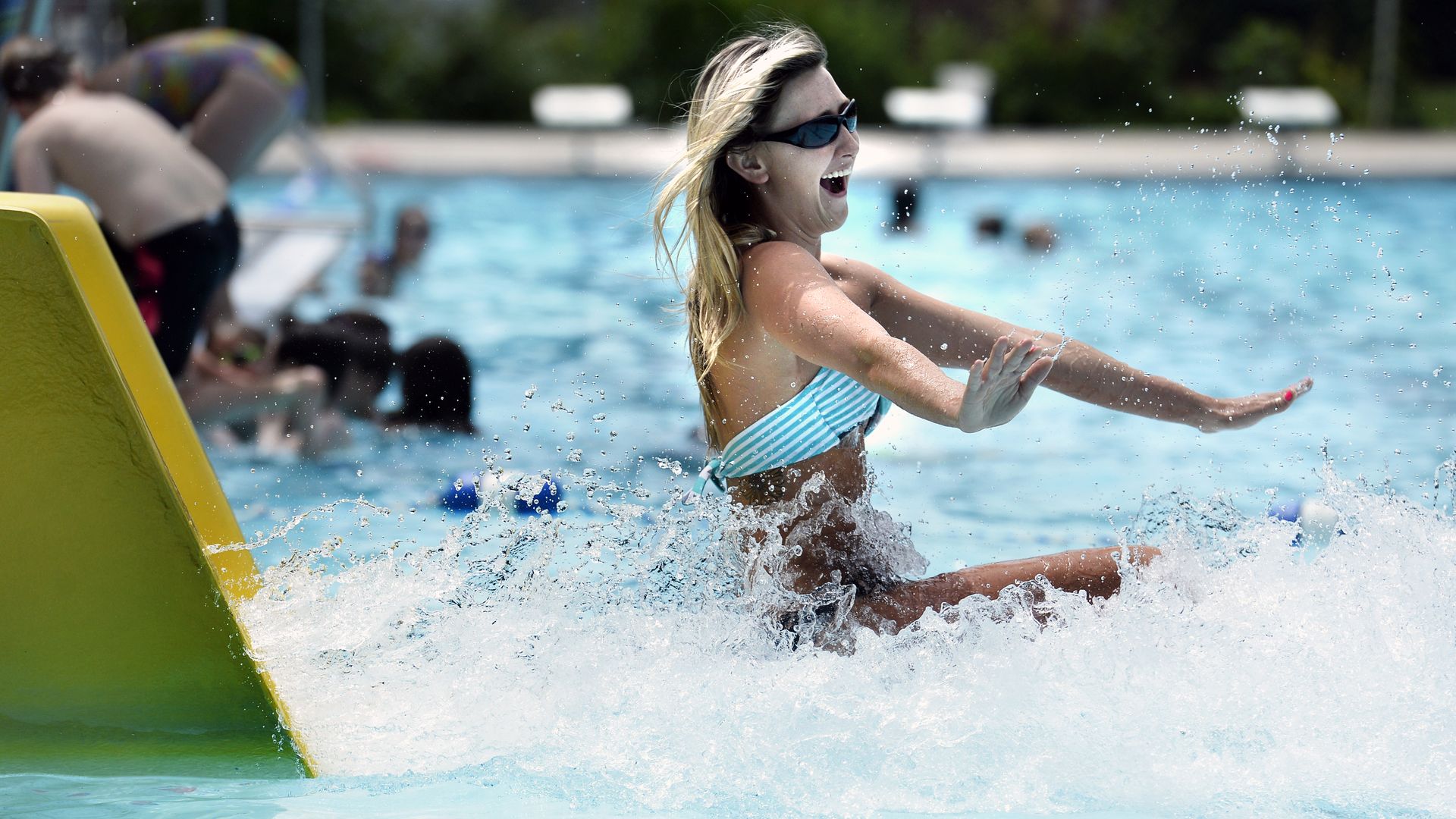A woman wearing sunglasses and a swimsuit smiles as she comes off of a water slide at Scott Carpenter Pool