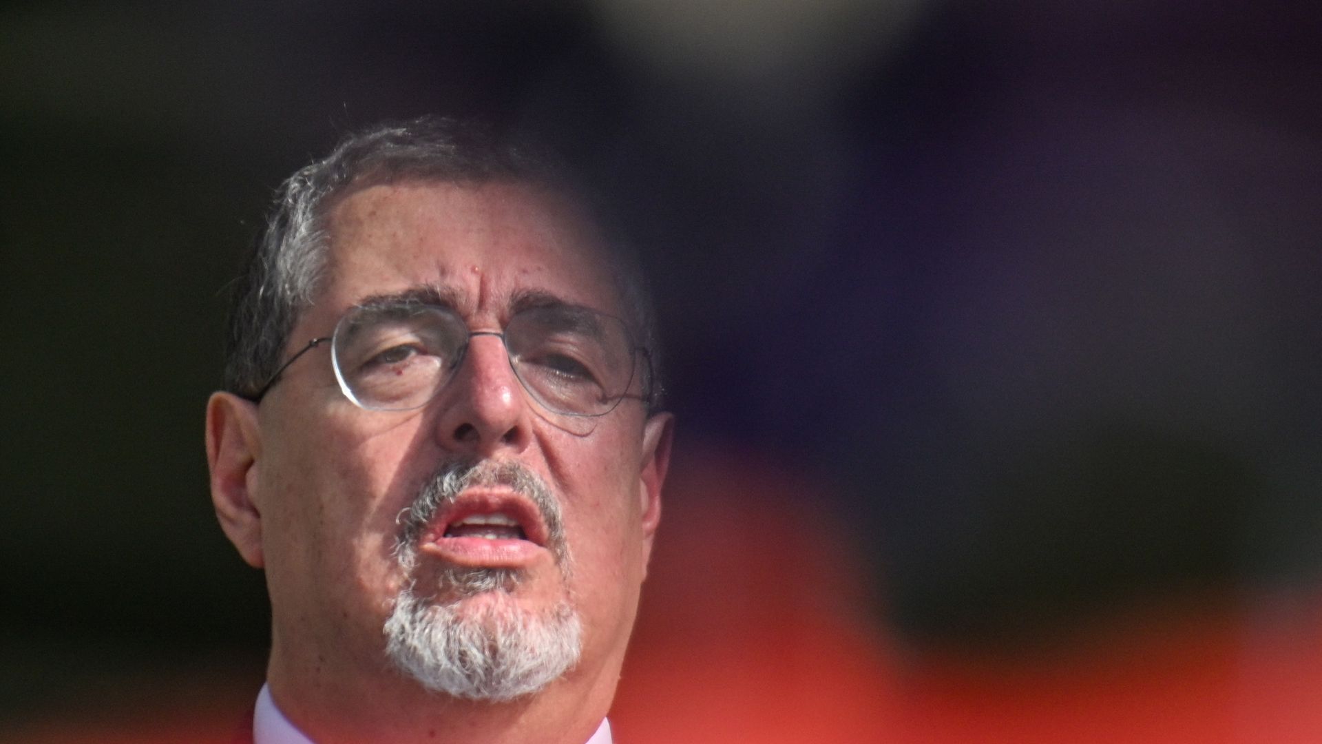 Guatemala President Bernardo Arévalo is shown close up, looking straight out,not smiling. there is a red orb under him. 