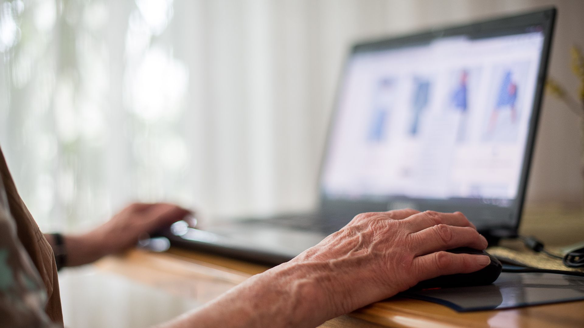 Elderly hand uses mouse and laptop.