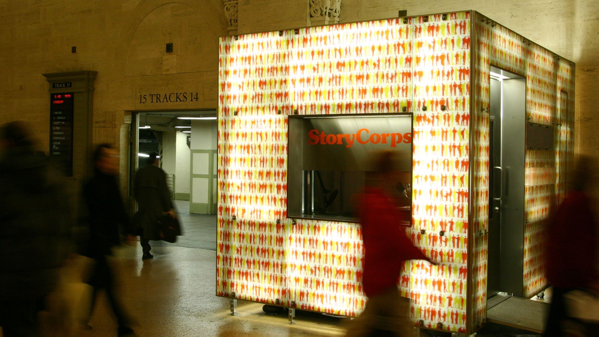 People in a train station walk by an illuminated both