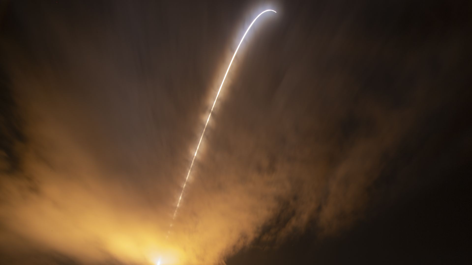 A rocket launches Nasa's Parker Solar Probe. It appears as a streak of light in a dark and gold sky. 
