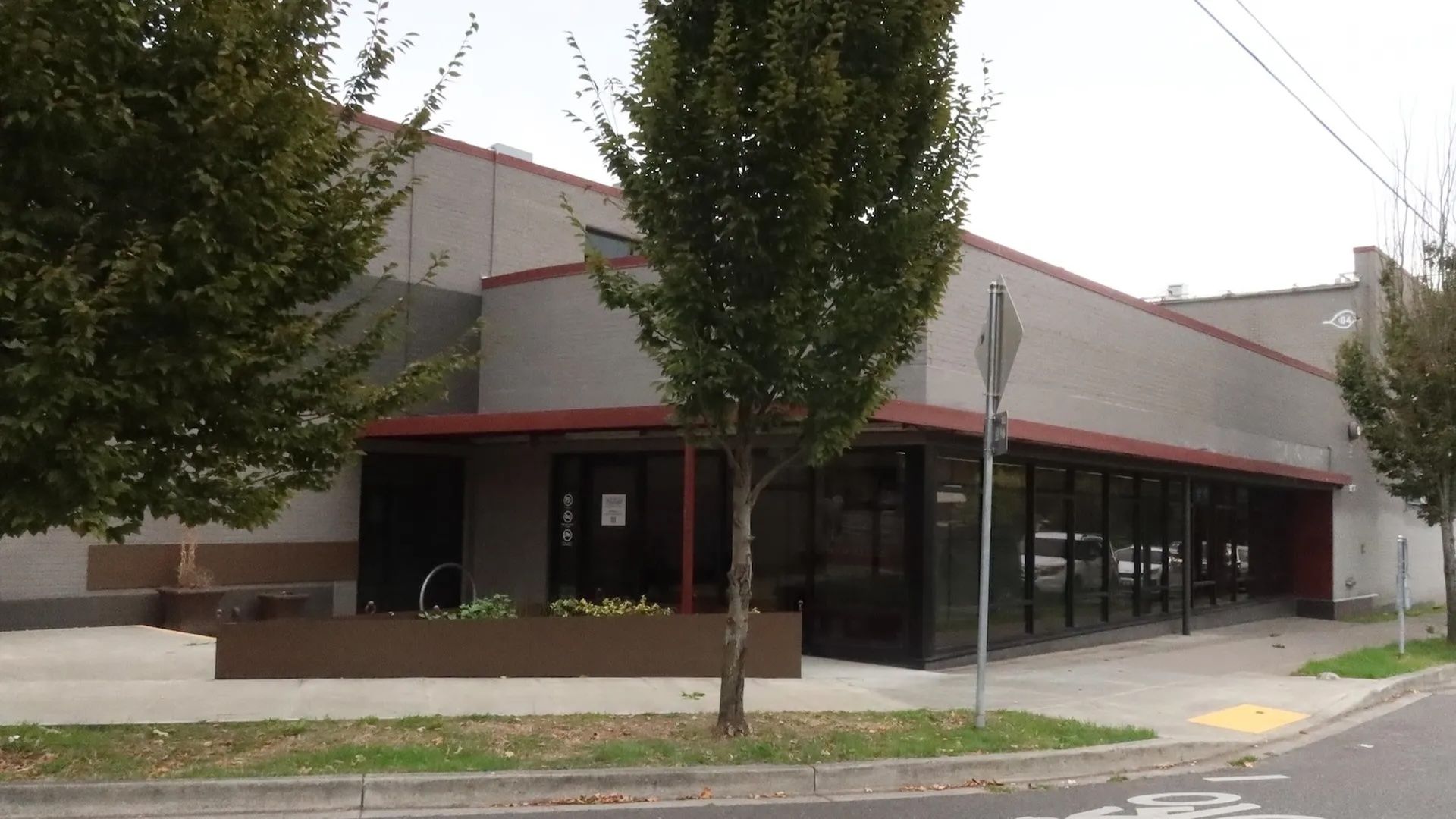 A photo of the outside of a gray building with several trees lined in front.