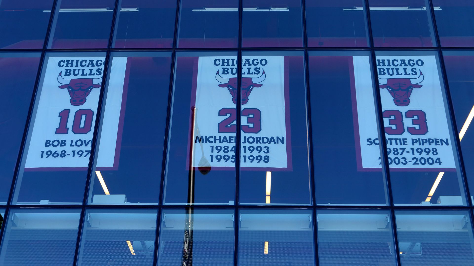 Photo of three banners hung up above a basketball court with numbers 10, 23 and 33 printed on them. 