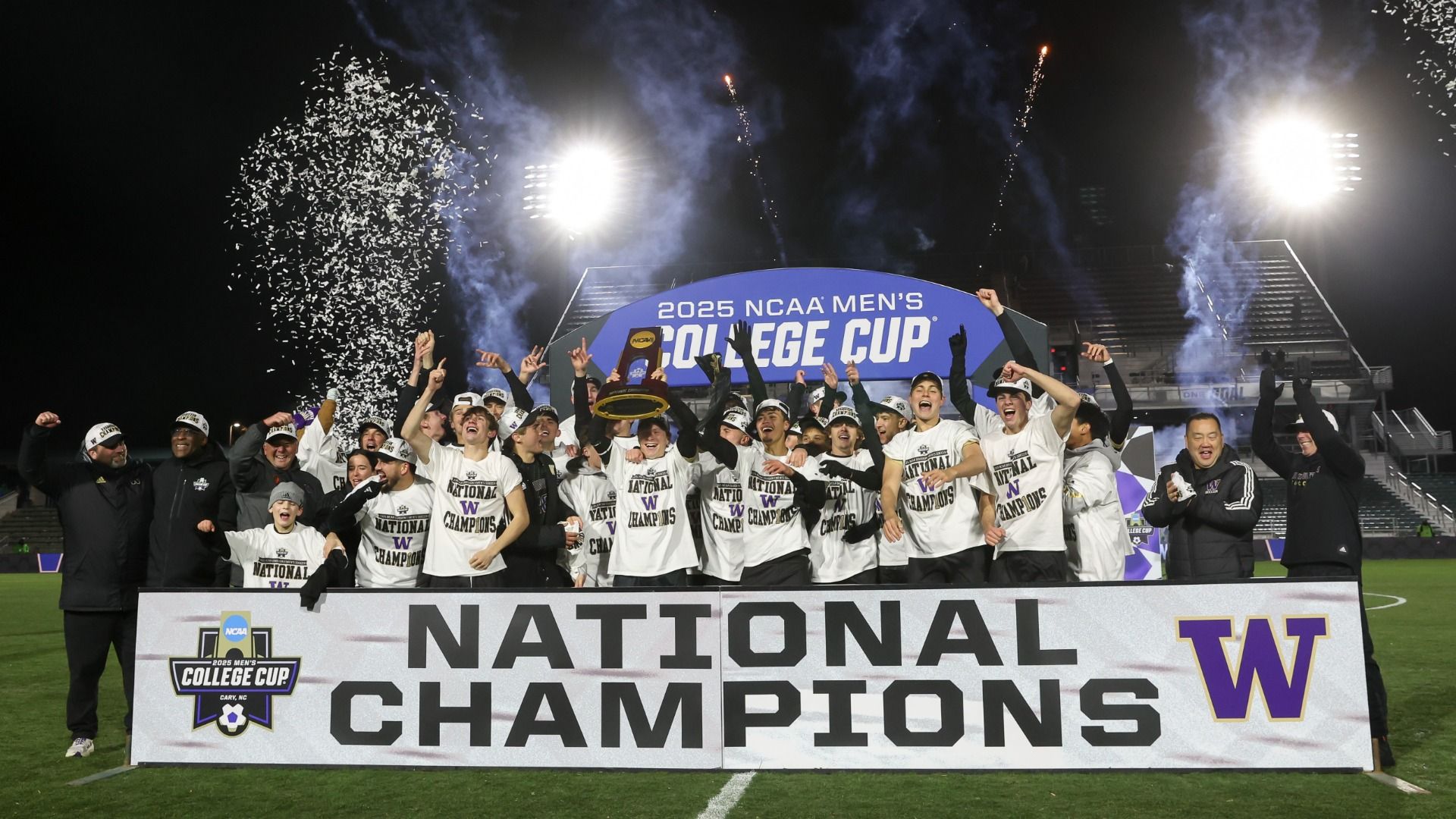 A banner reading "national champions" with the University of Washington logo sits in the foreground, with team members cheering behind it and confetti and fireworks blasting.