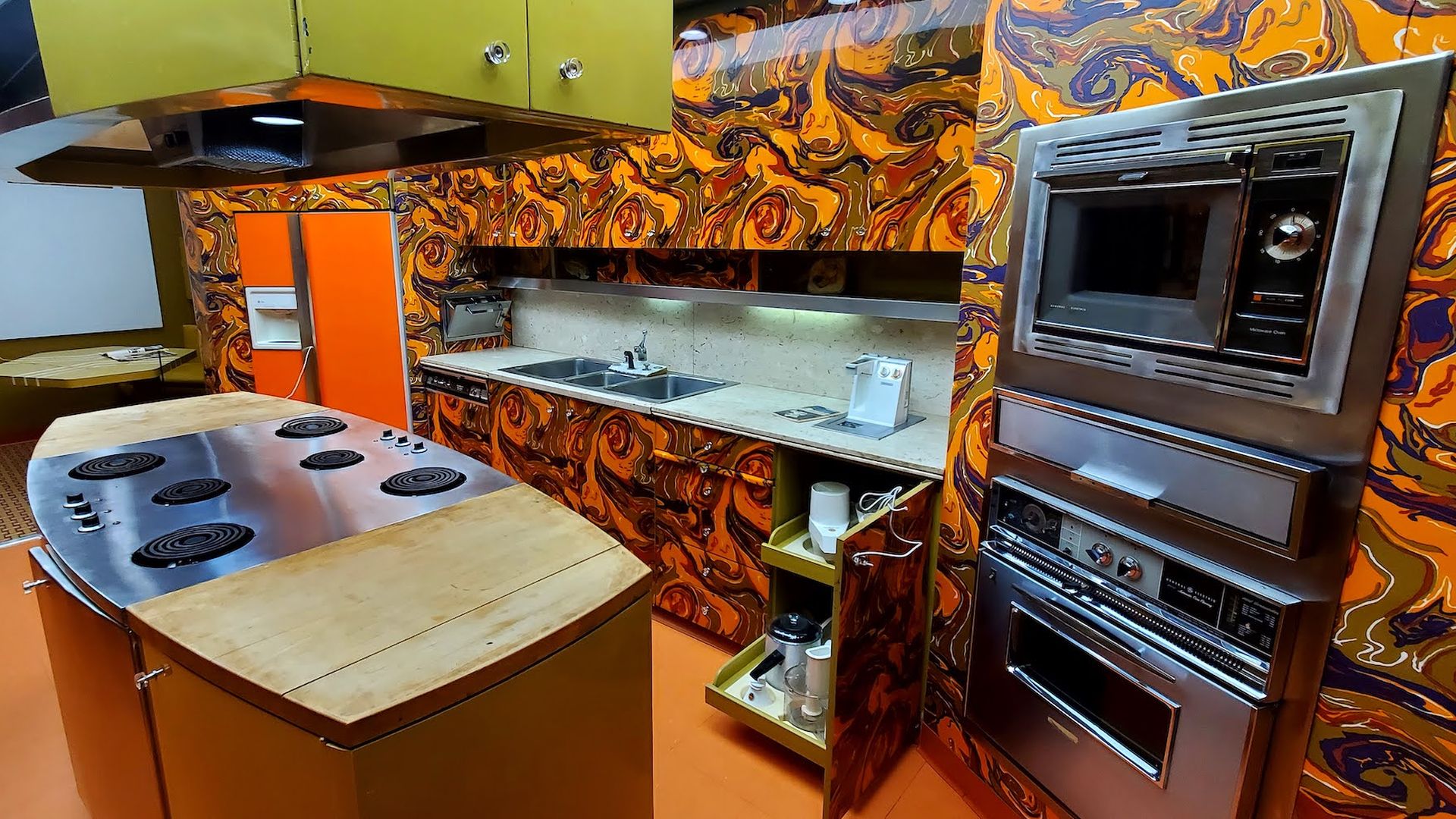 Orange and brown paisley walls, upper and lower ovens, stovetop and lime green range in Ebony Test Kitchen.