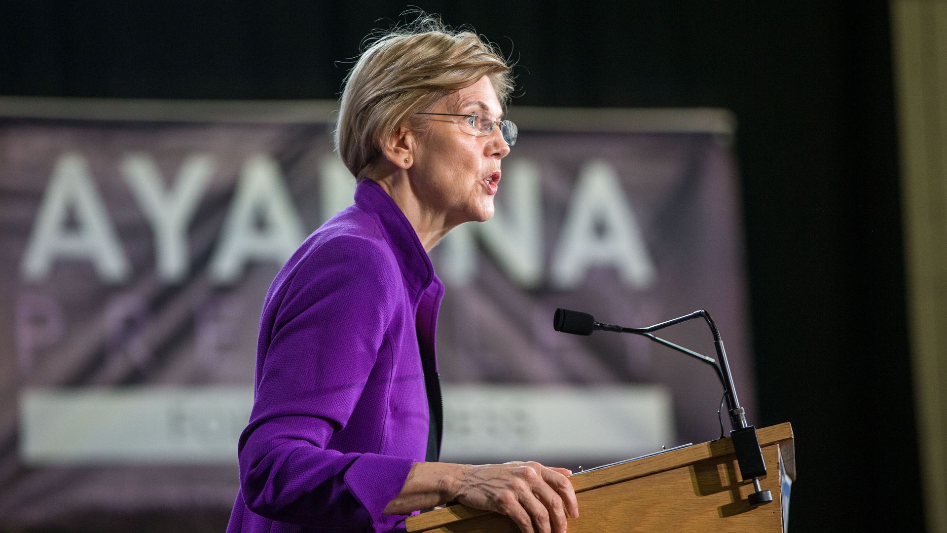 Elizabeth Warren stands at a podium on stage. 