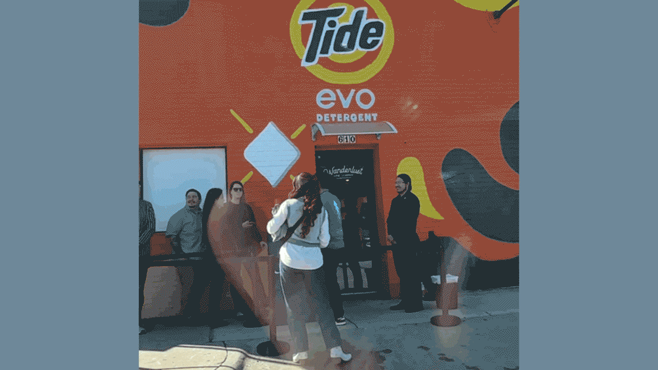 moving image of a long line of people outside of a small building decorated with Tide branding