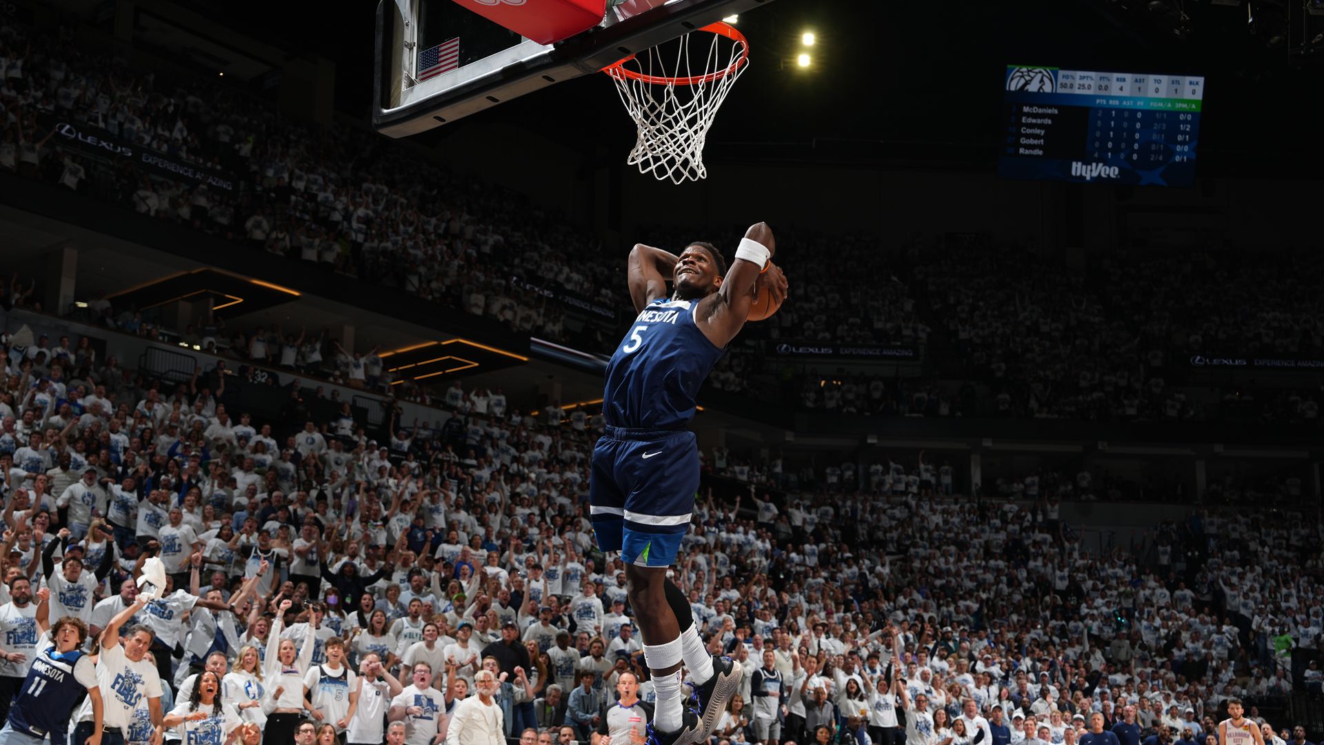 Anthony Edwards jumping in the air with a basketball behind his head, flying toward the rim. Behind him are fans at Target Center wearing white shirts, 