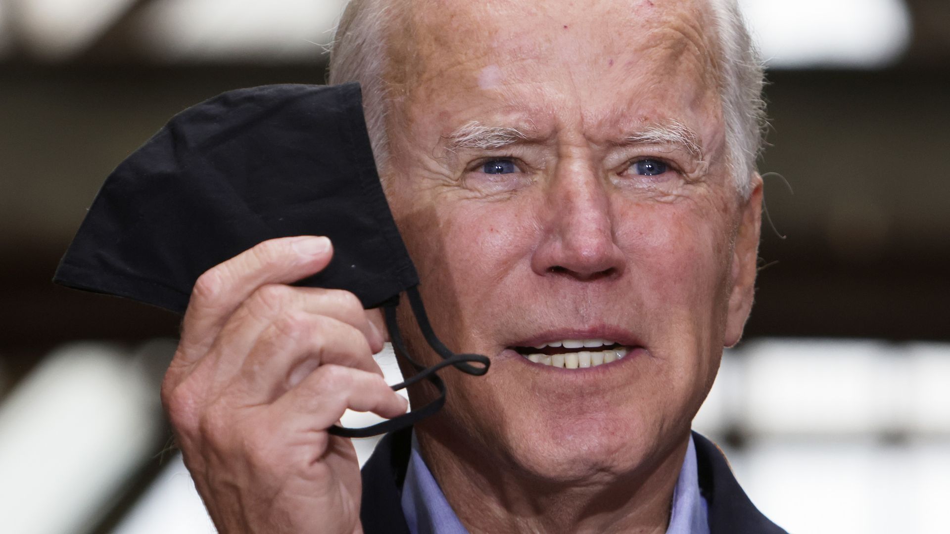 Joe Biden with a mask in his right hand next to his face