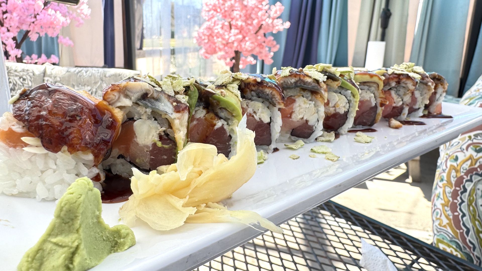 A long plate with a sushi roll topped with avocado and eel sauce.  