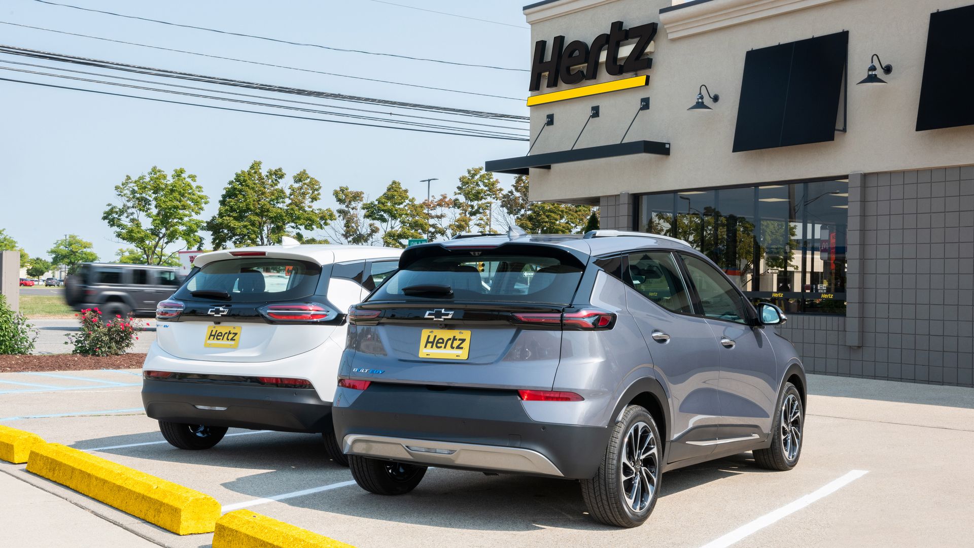 Two Chevy Bolts sit outside a Hertz rental office.