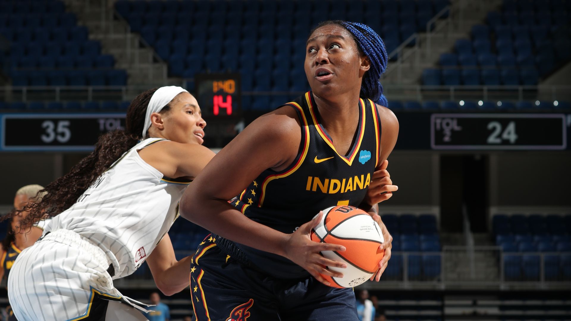 Aliyah Boston holds a basketball while looking to the left, evading a Chicago Sky defender. 