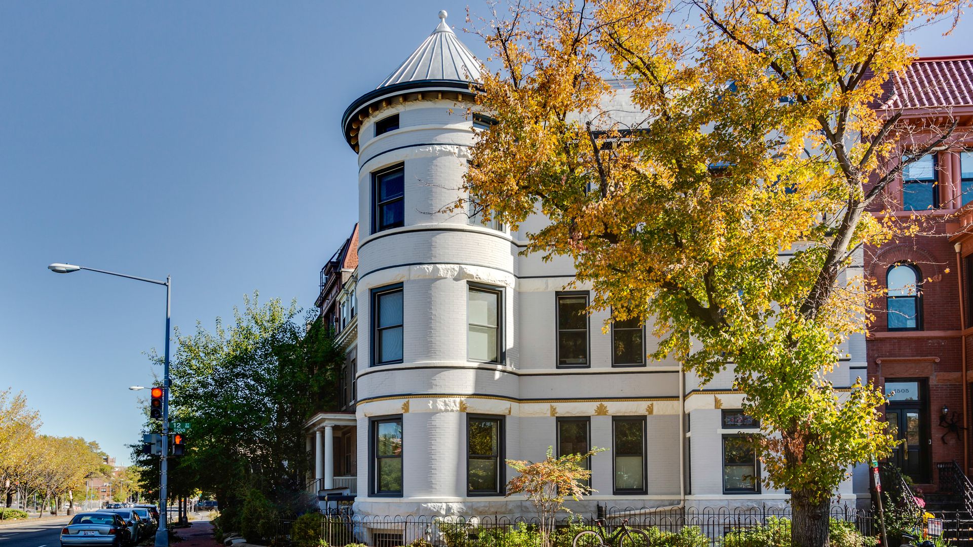 The outside of a white Victorian home that's been converted into condos with a tree out front.
