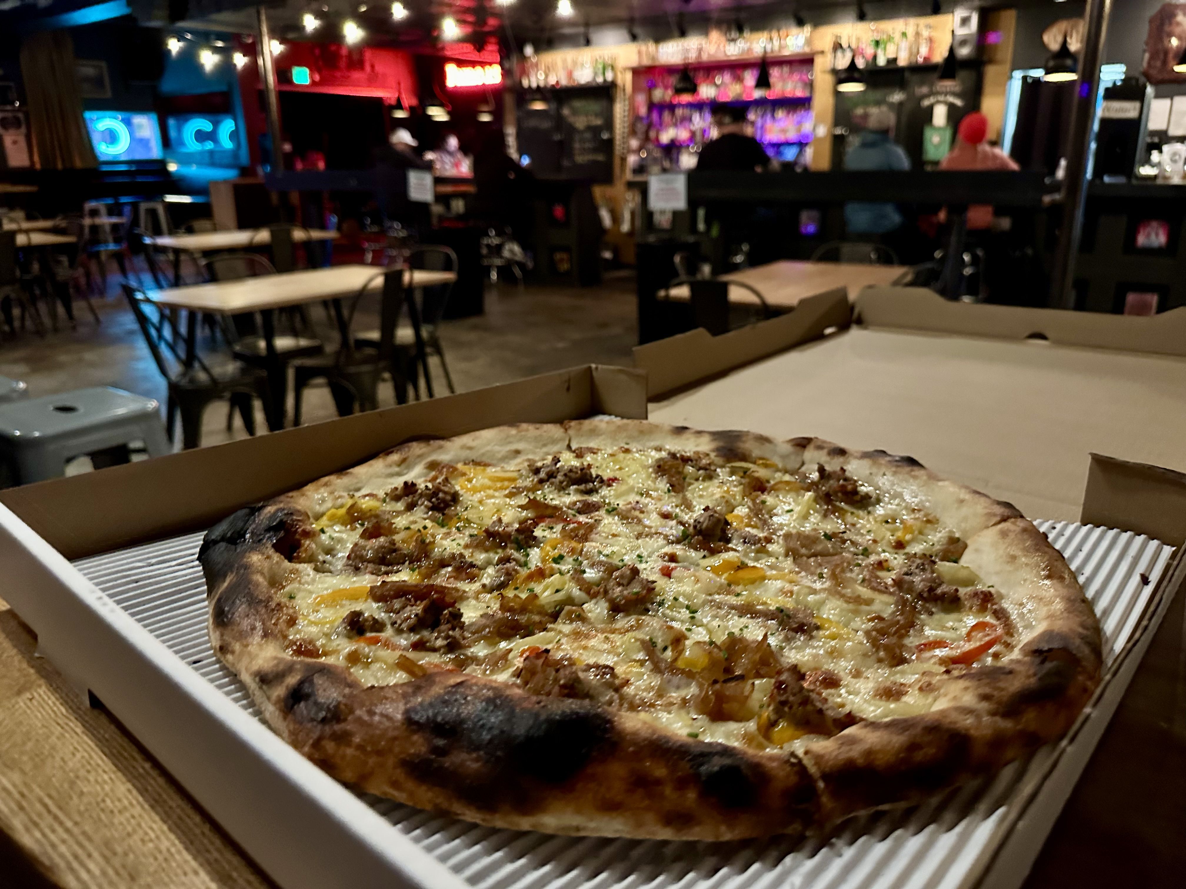 A pizza with sausage, onions and pickled peppers on a bar table with the bar shown in the background.