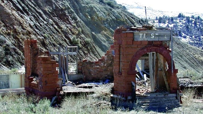 A ruined building of red stone with an arch and a sign that reads "Thistle"